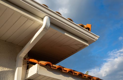 House corner with white planks siding and roof with steel gutter rain system and pipes installation